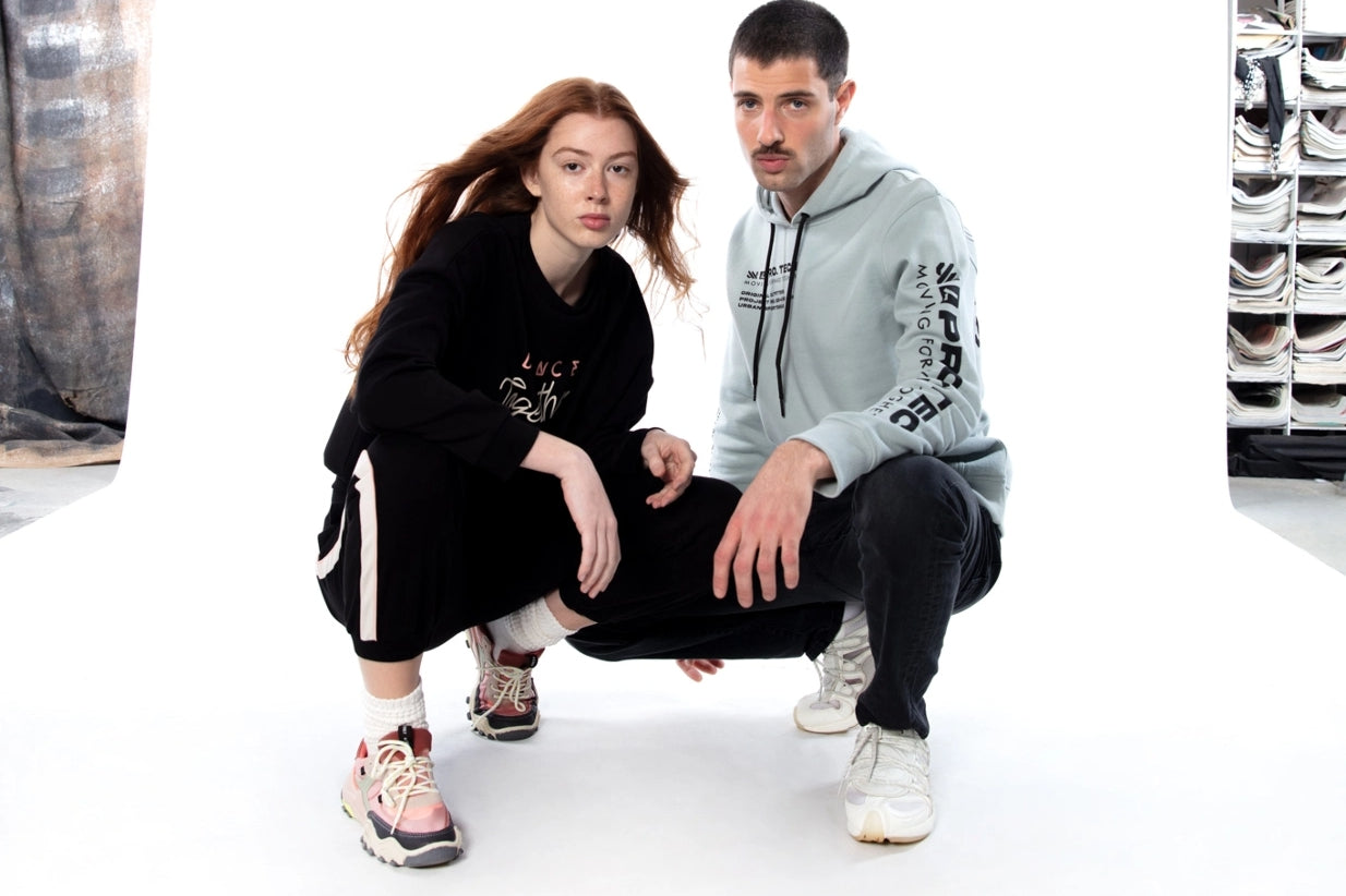 Man wearing a black hoodie with stripped pants crouching next to a crouching man wearing a grey hoodie with black pants