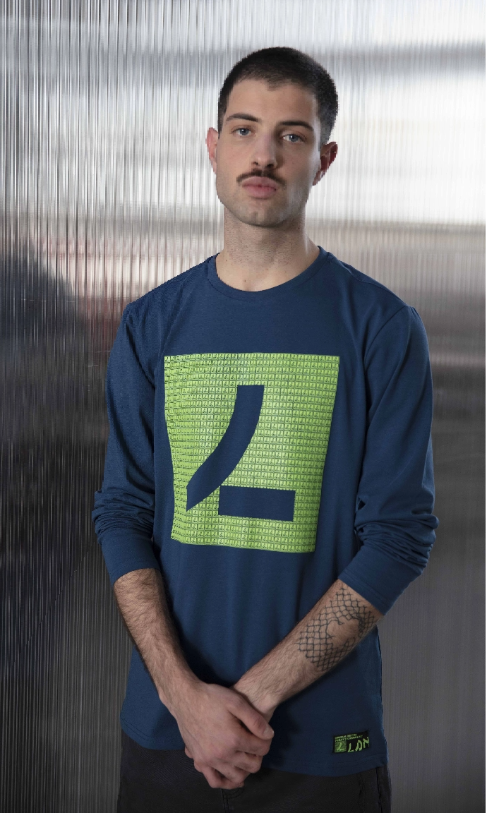 Man standing up next to glass wall, wearing blue sweat with LOSAN logo in light green