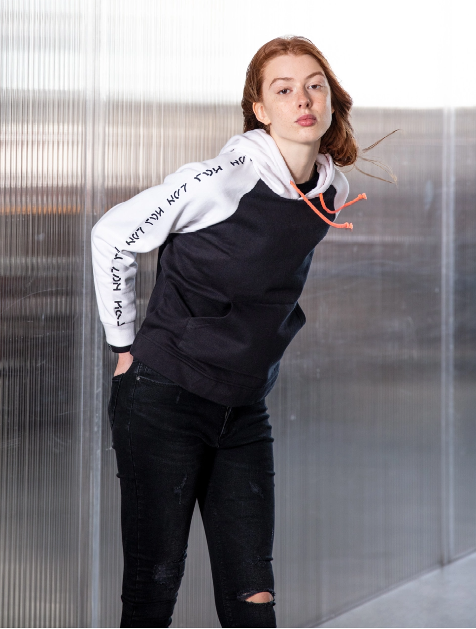 Woman leaning against glass wall, wearing a black and white hoodie