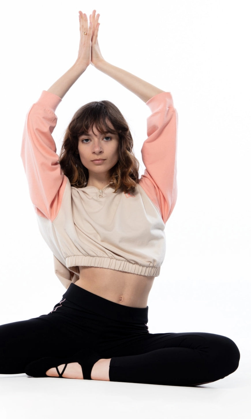 woman sitting on floor with arms above head in a yoga position wearing a white and pink hoodie