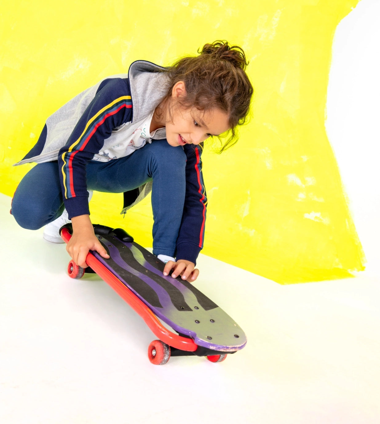 Kid playing with a skateboard wearing a multicolored jacket
