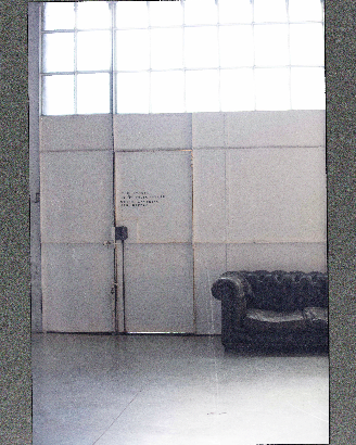 Photographic set, displaying a room with a closed door with a sentence written in black lettering next to a empty black couch