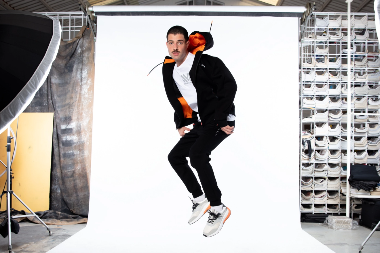 Hombre saltando en un set fotográfico con una sudadera con capucha naranja y pantalones negros