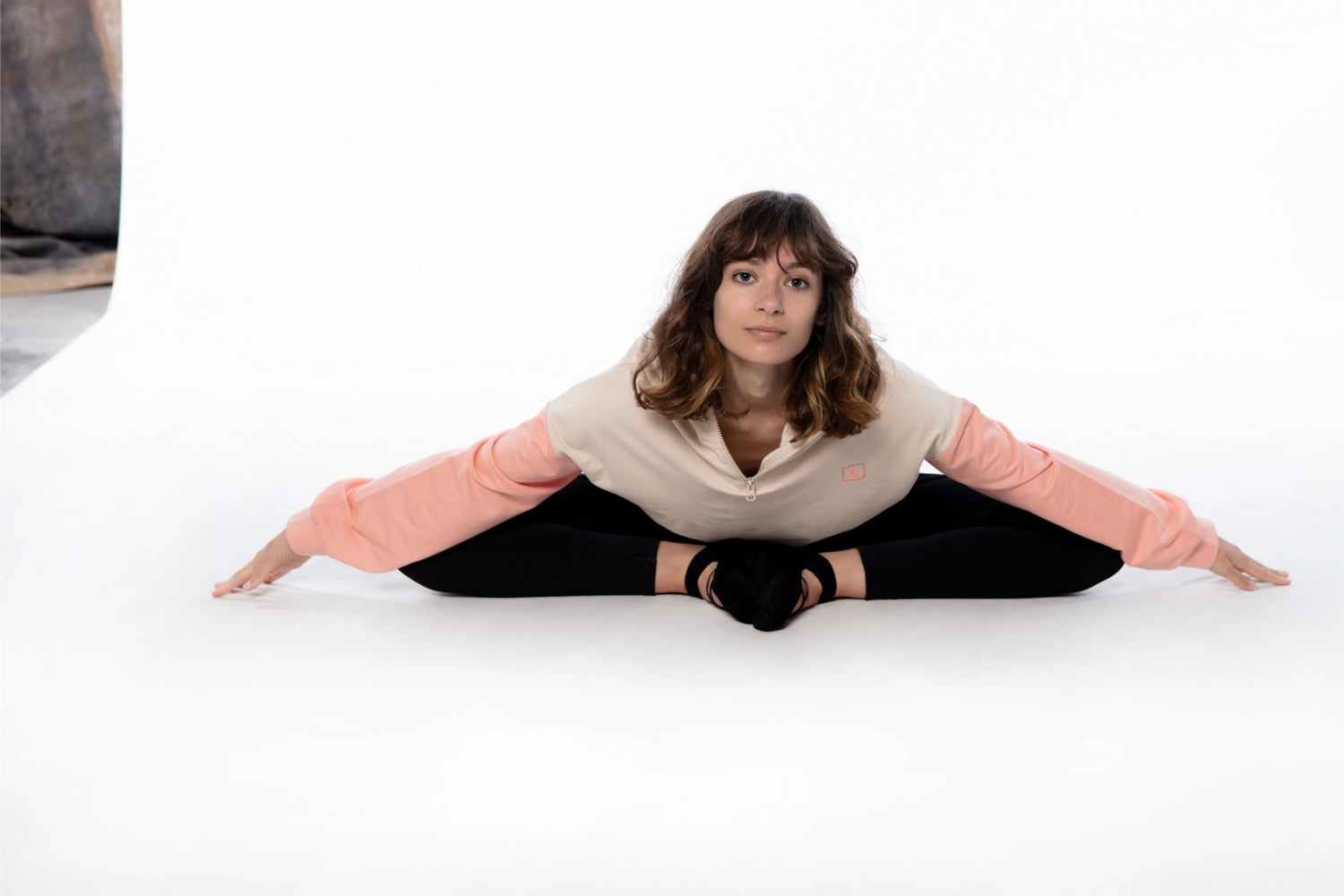 Woman sitting on floor in a yoga position wearing a pink hoodie and black leggings