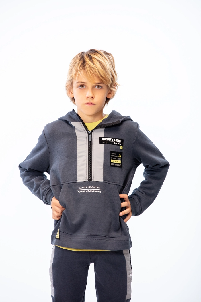 Kid standing up looking at camera wearing a zipped up grey and white hoodie
