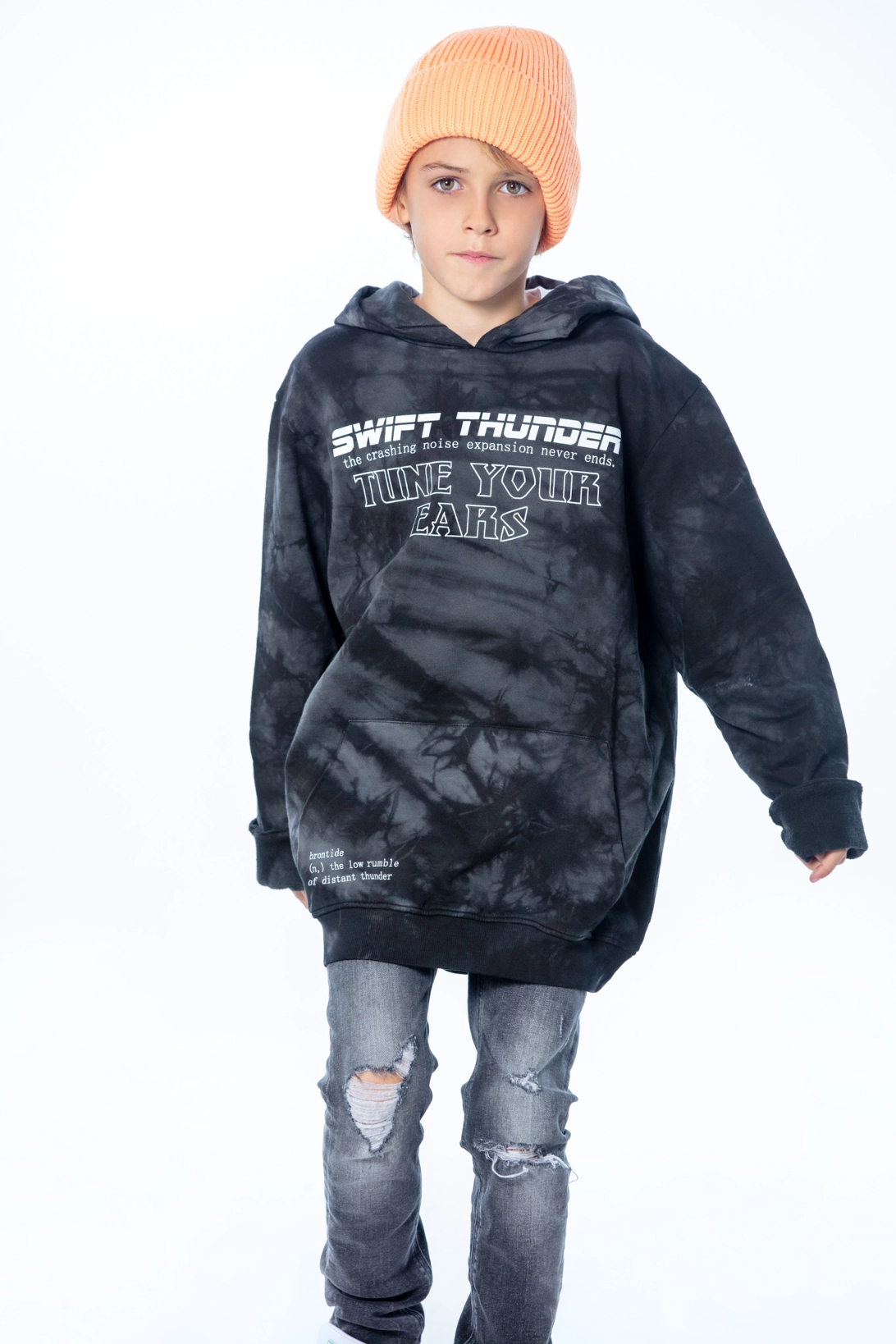 Kid walking towards camera wearing a black hoodie with printed lettering and ripped jeans