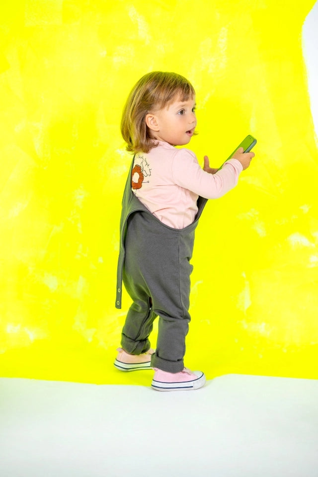 Side profile of a toddler playing around wearing grey overalls and pink sweat