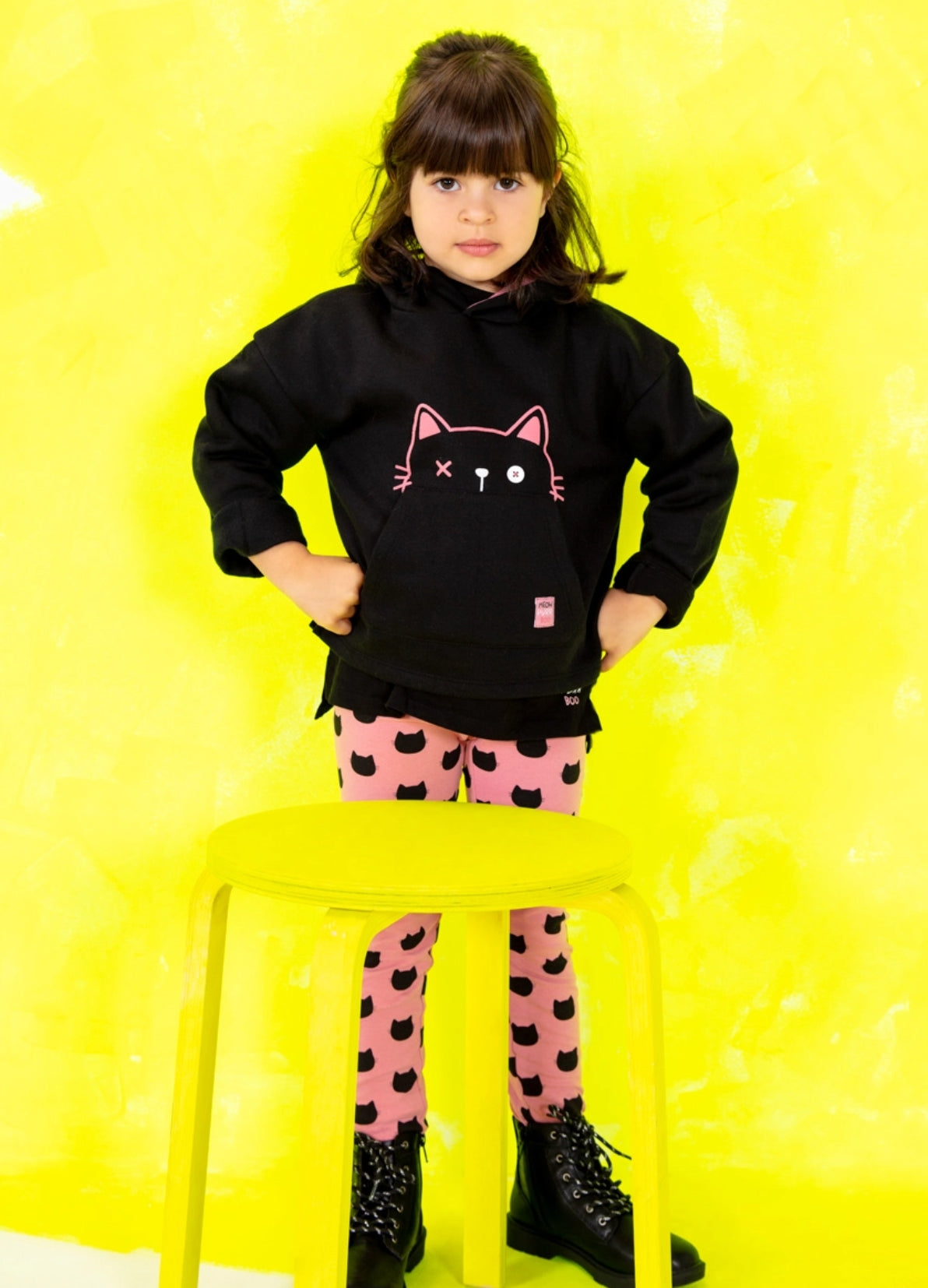 LOSAN - Happy Black a collection, kid standing up next to yellow bench wearing a pink and black combo of sweat and printed leggings