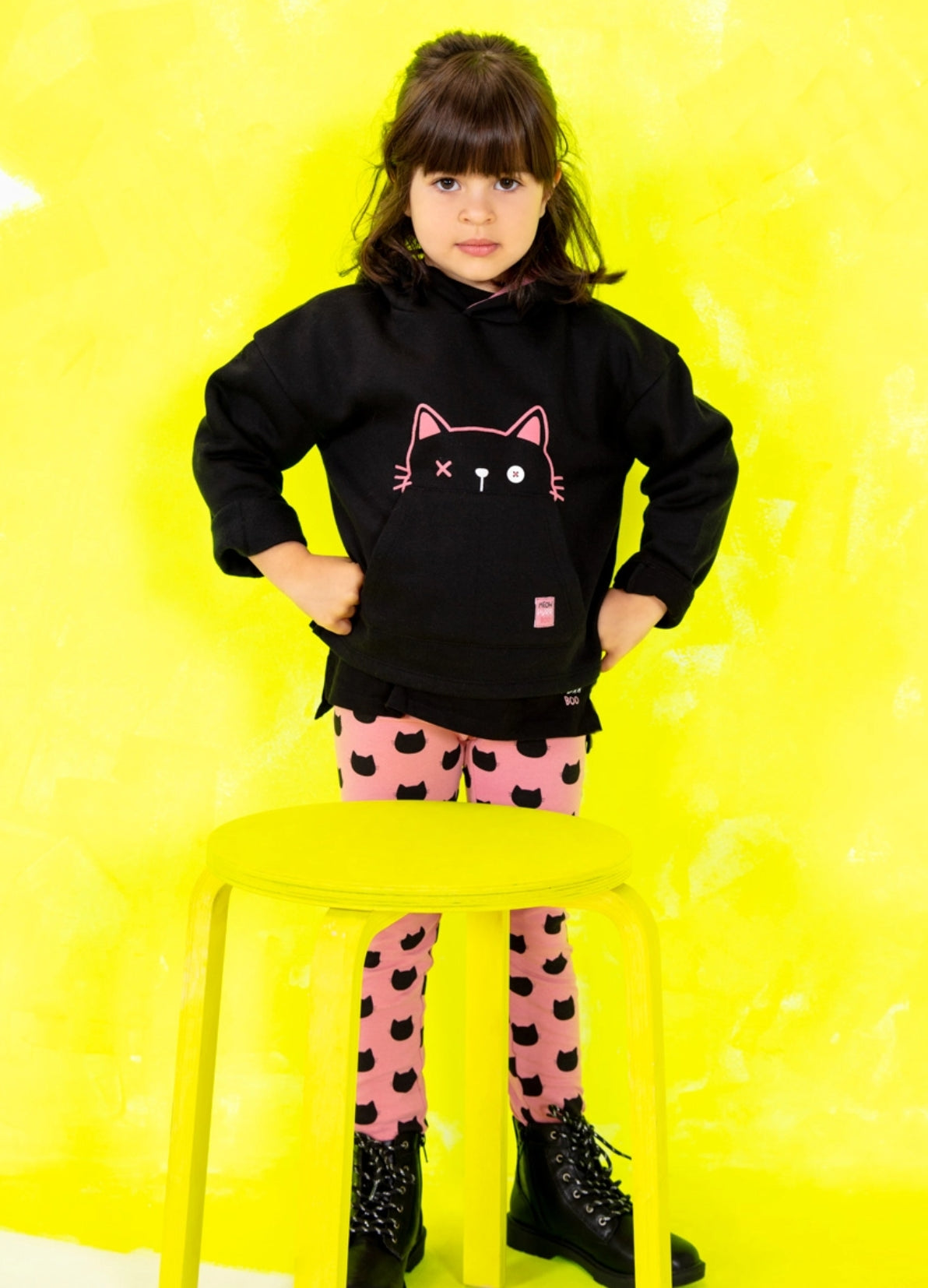 LOSAN - Happy Black a collection, niño de pie junto a un banco amarillo con una combinación rosa y negra de sudor y calzas estampadas