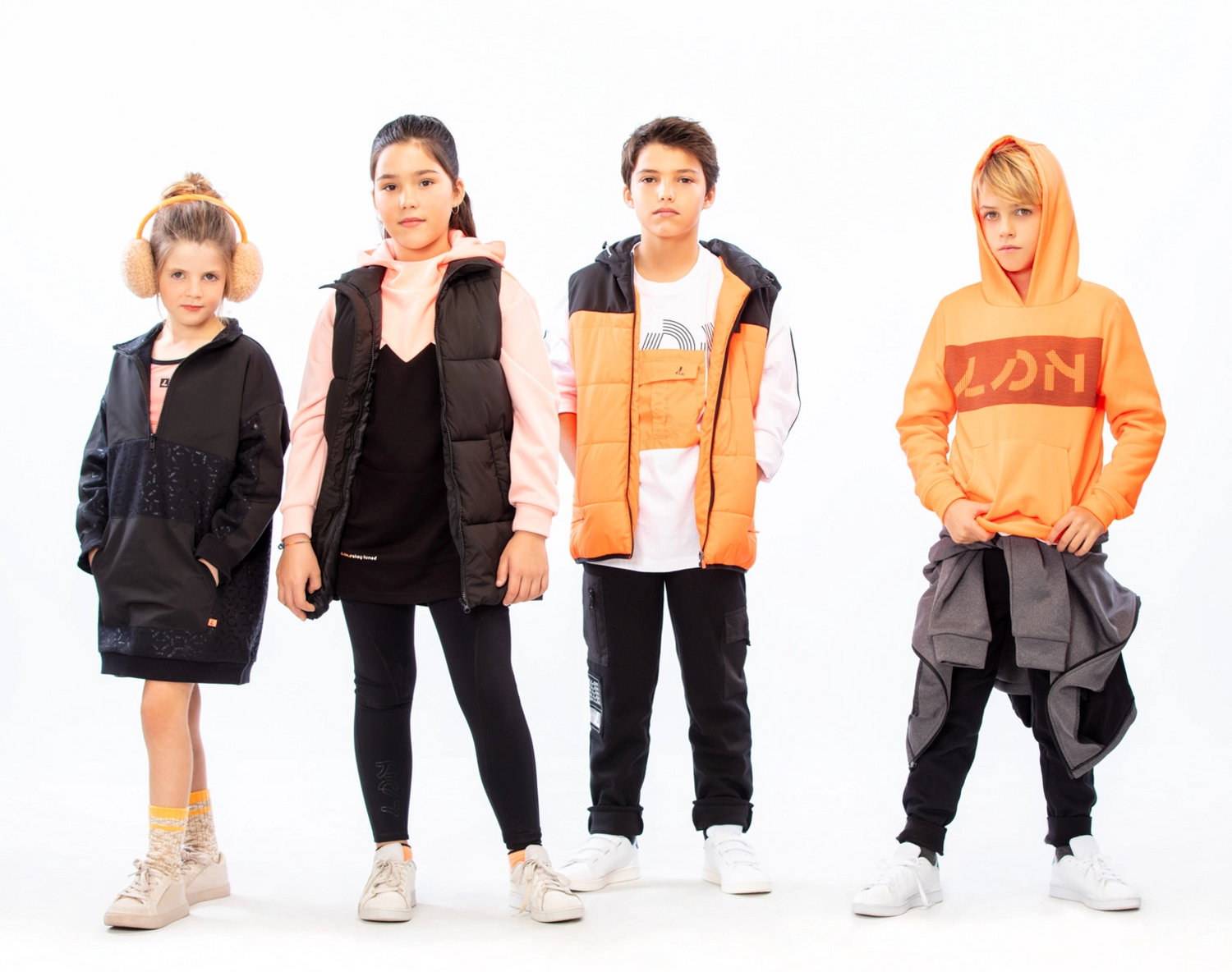 Four kids standing in a line next to each other, wearing black and orange colored clothing