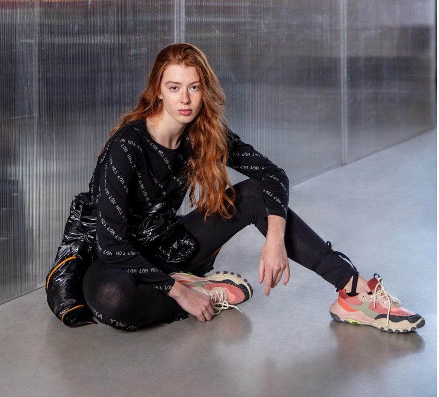 woman sitting against a glass wall, wearing a printed shirt and black leggings