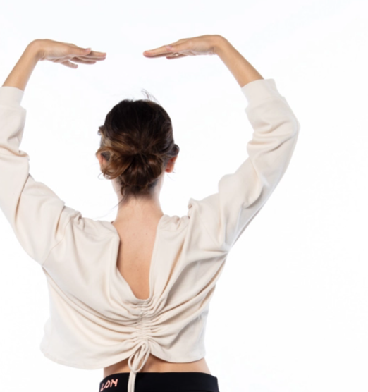 Back view of a woman with arms above head wearing a white open back top