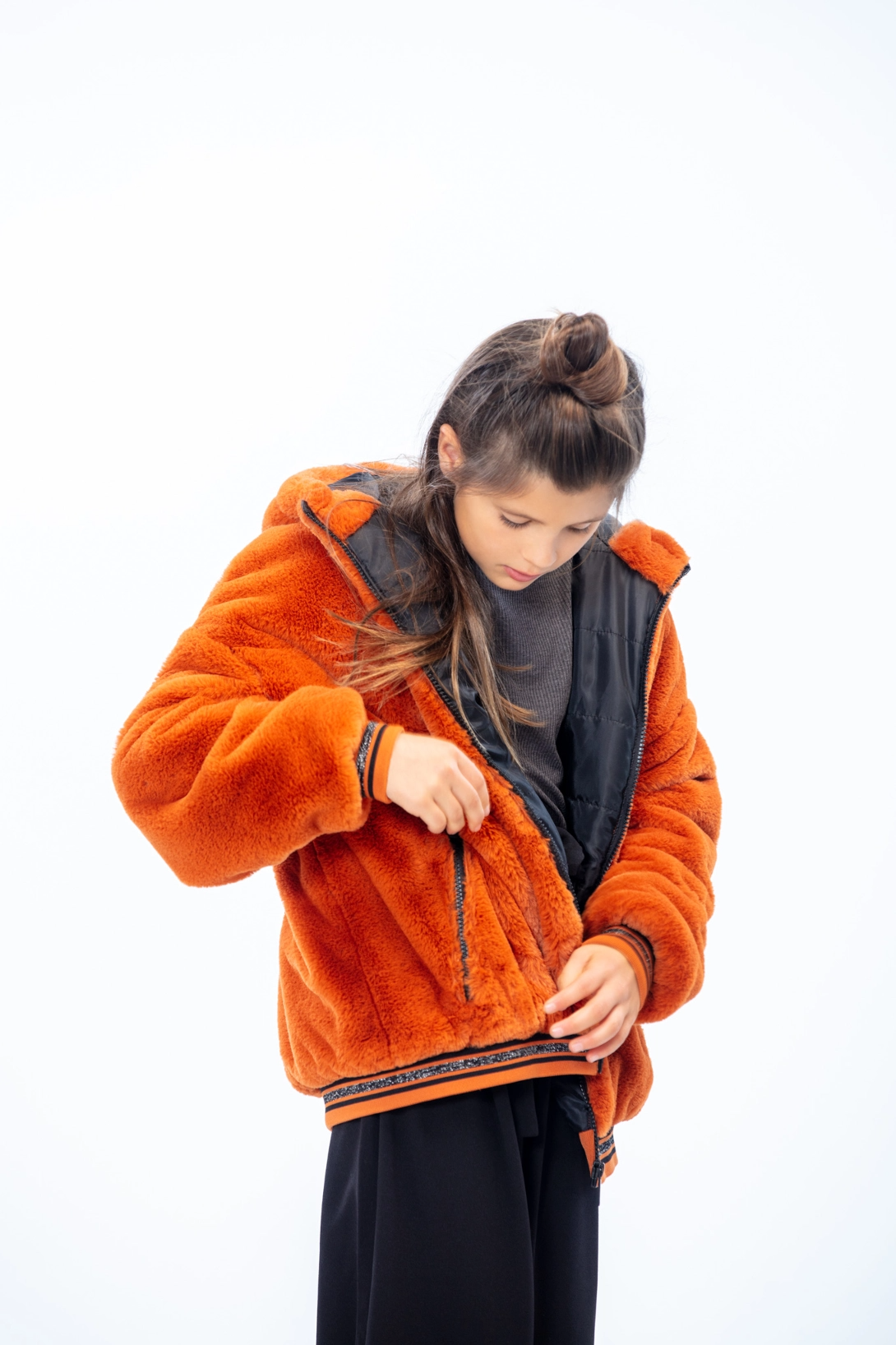 side profile of a kid standing up closing her orange jacket pocket, with a black  shirt and pants